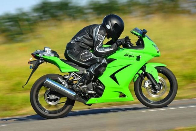 Зеленая Kawasaki Ninja 250 под управлением мотоциклиста в черном комбинезоне