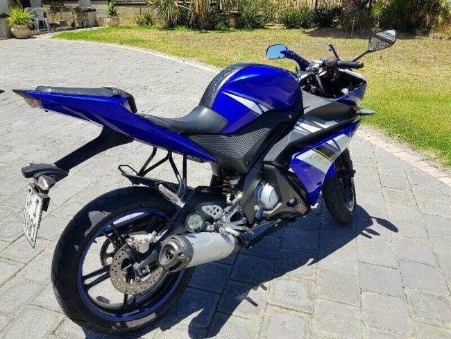 Вид сзади синего мотоцикла Yamaha YZF-R125 с довольно крупным глушителем