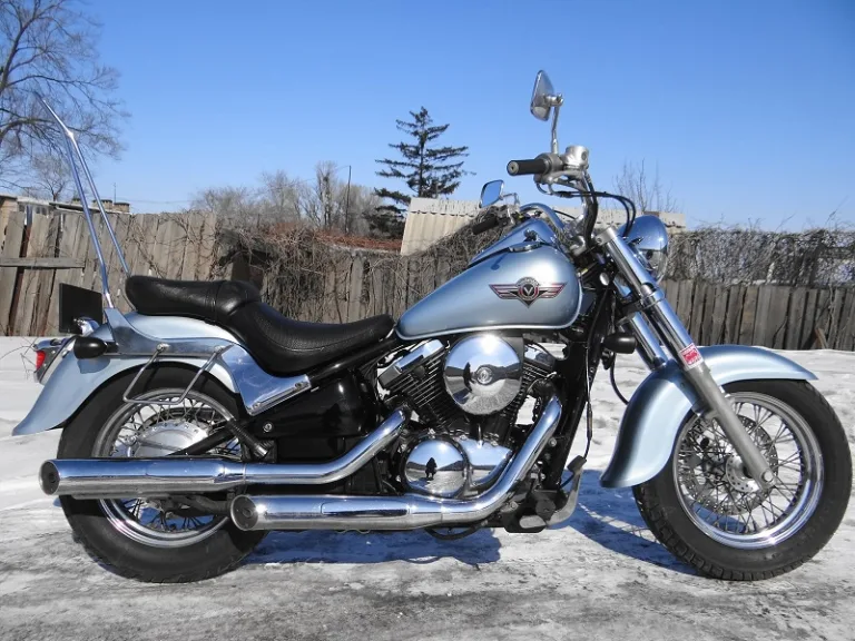 Серебристый мотоцикл Kawasaki Vulcan VN 400 на фоне снега во дворе частного дома