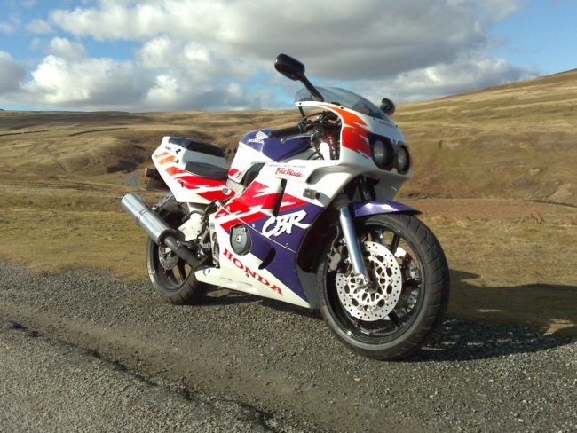 Внешний вид спортивного мотоцикла Honda CBR400RR на фоне холмистой местности