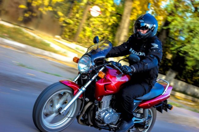 Мотоциклист в черном шлеме на малиновом байке Honda CB 500