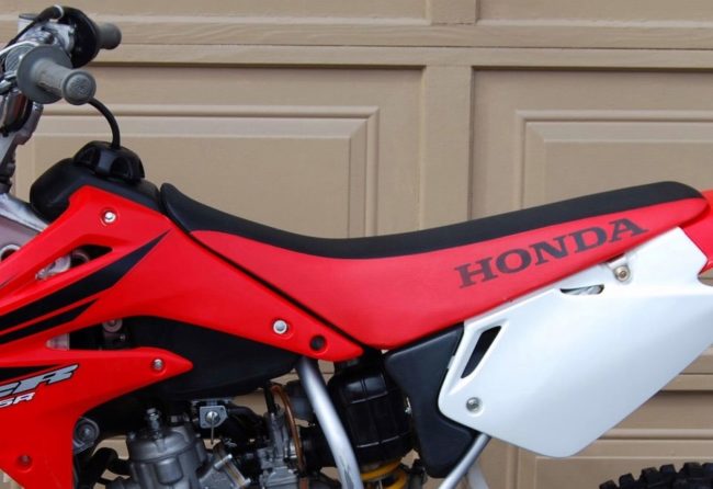 Узкое седло красно-черной расцветки на мотоцикле Honda CR85 кроссового класса